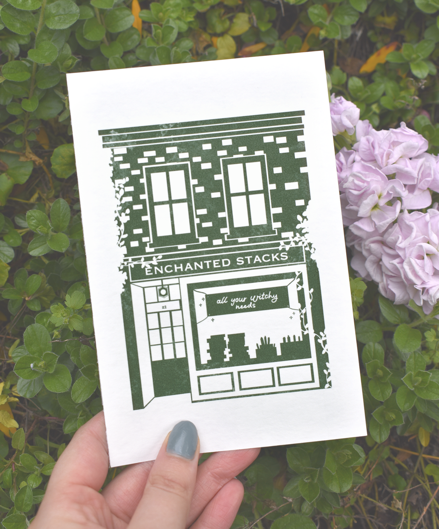 Art Print with 'Enchanted Stacks' design held over green foliage and flowers