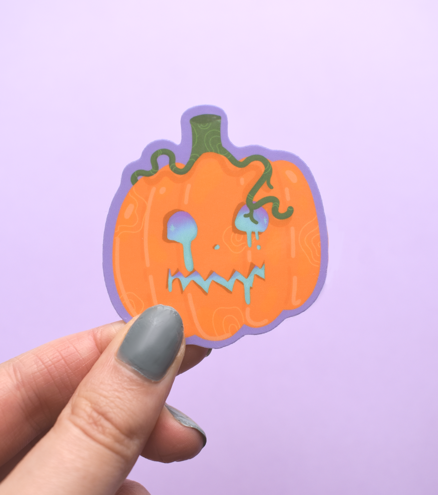 Hand holding a jack-o'-lantern sticker against a purple background