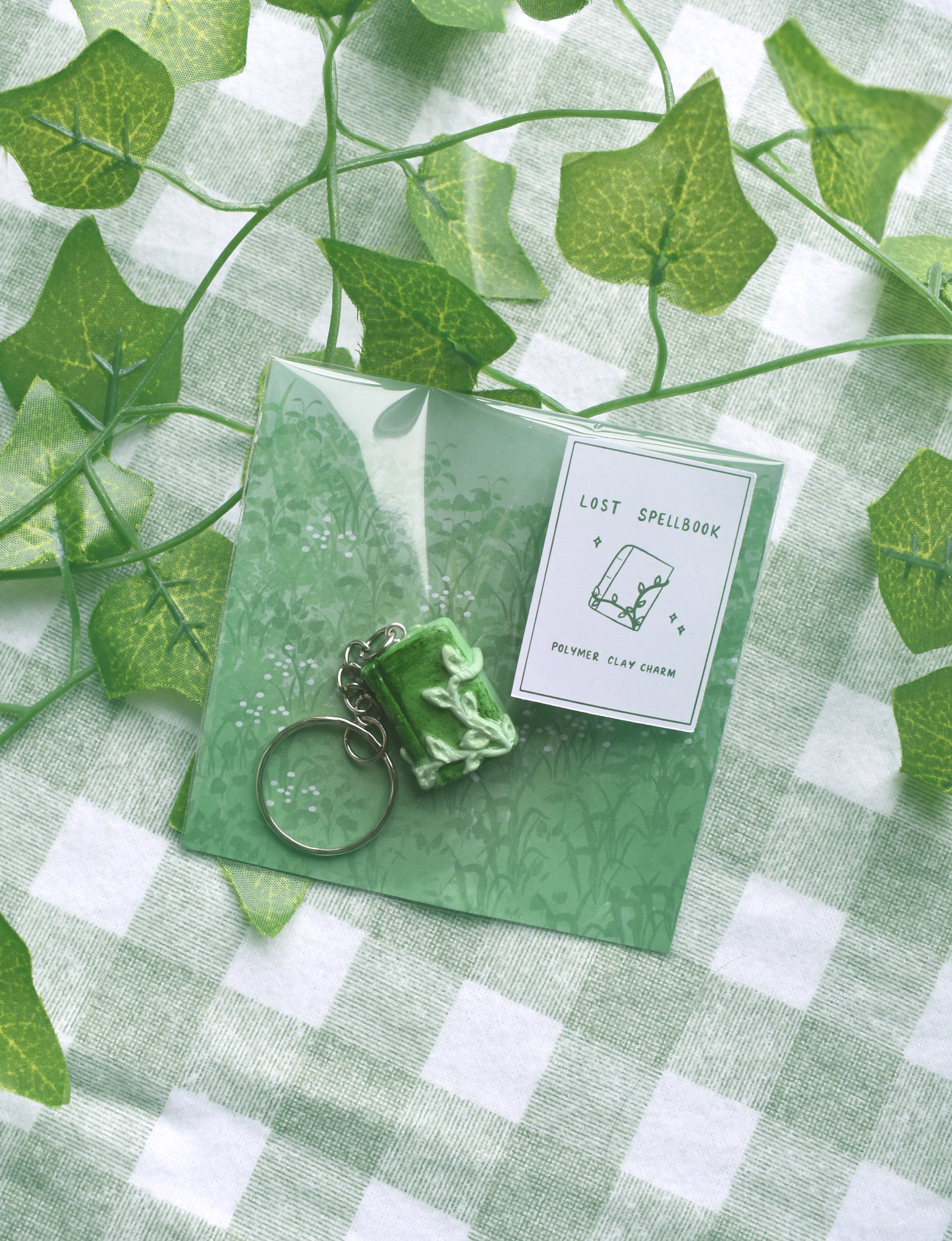 Green keychain and card on a green checkered fabric background with ivy leaves.