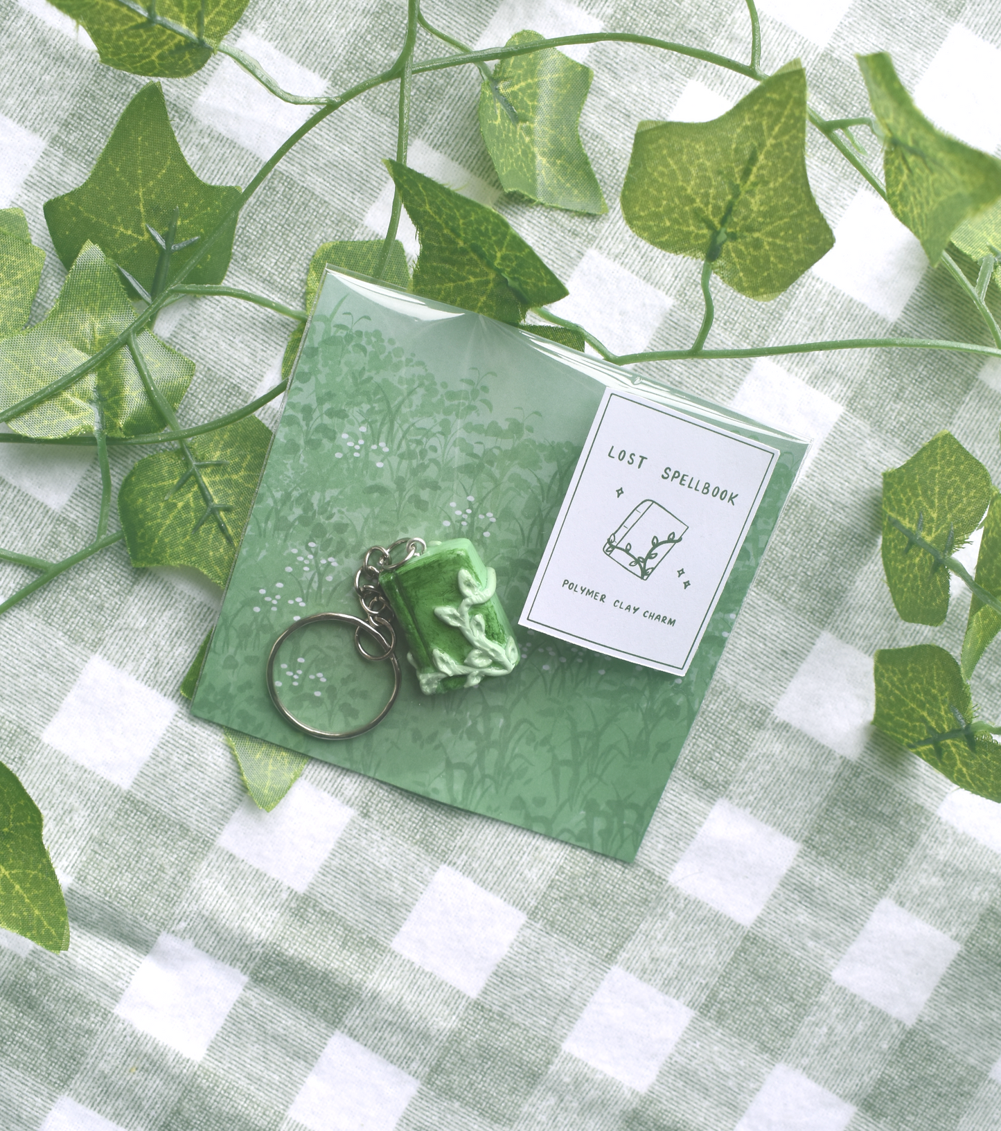 Green keychain and card on a green and white checkered fabric background with leaves.