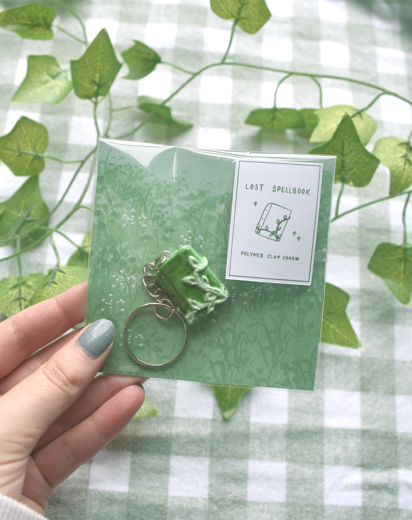 Green keychain with packaging held by a hand against a green and white checkered background