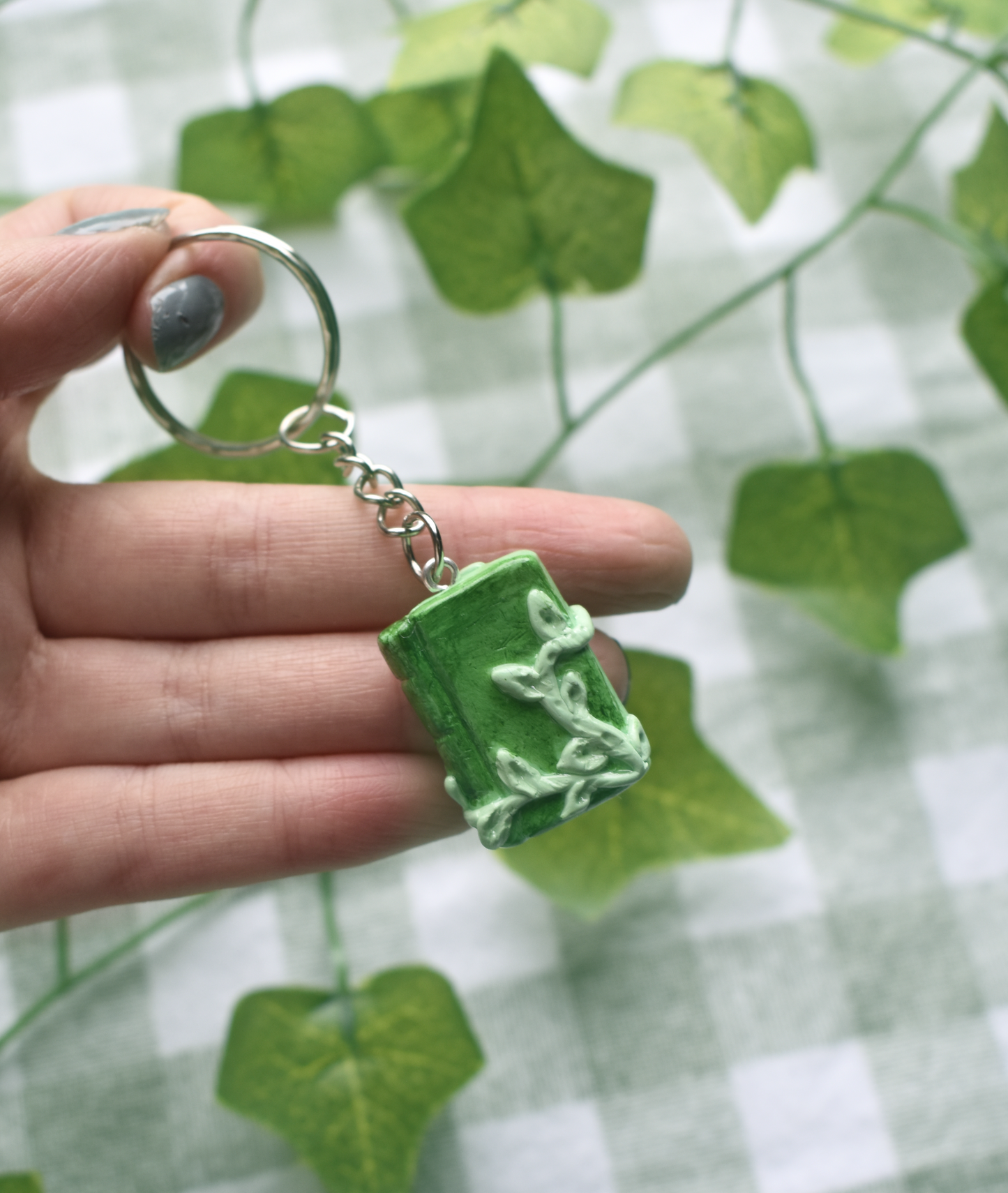 Hand holding a green keychain with a leaf design against a green leafy background
