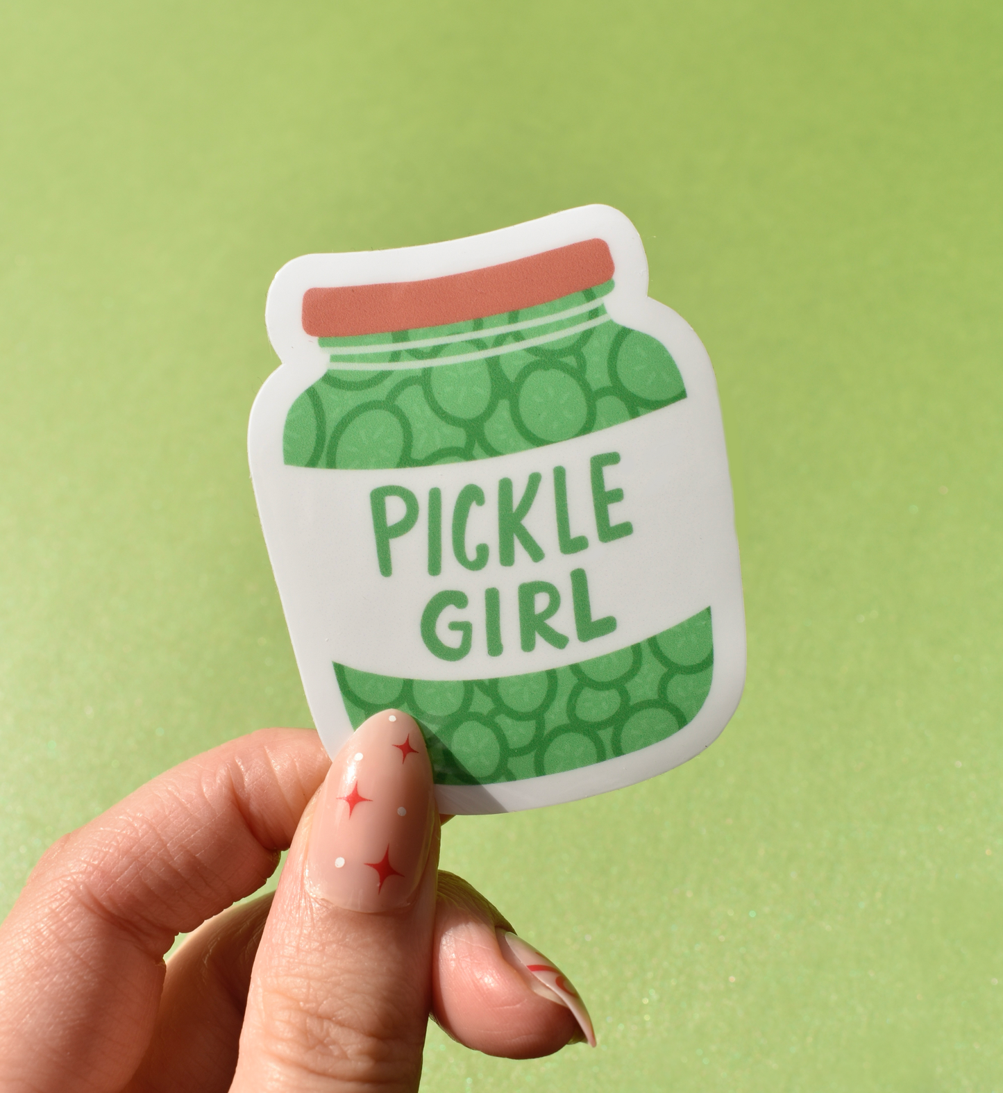Sticker of a pickle jar with 'Pickle Girl' text held by a hand against a green background