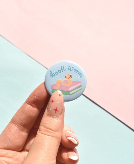 Button badge with 'Book Worm' design held by a hand on a pastel background