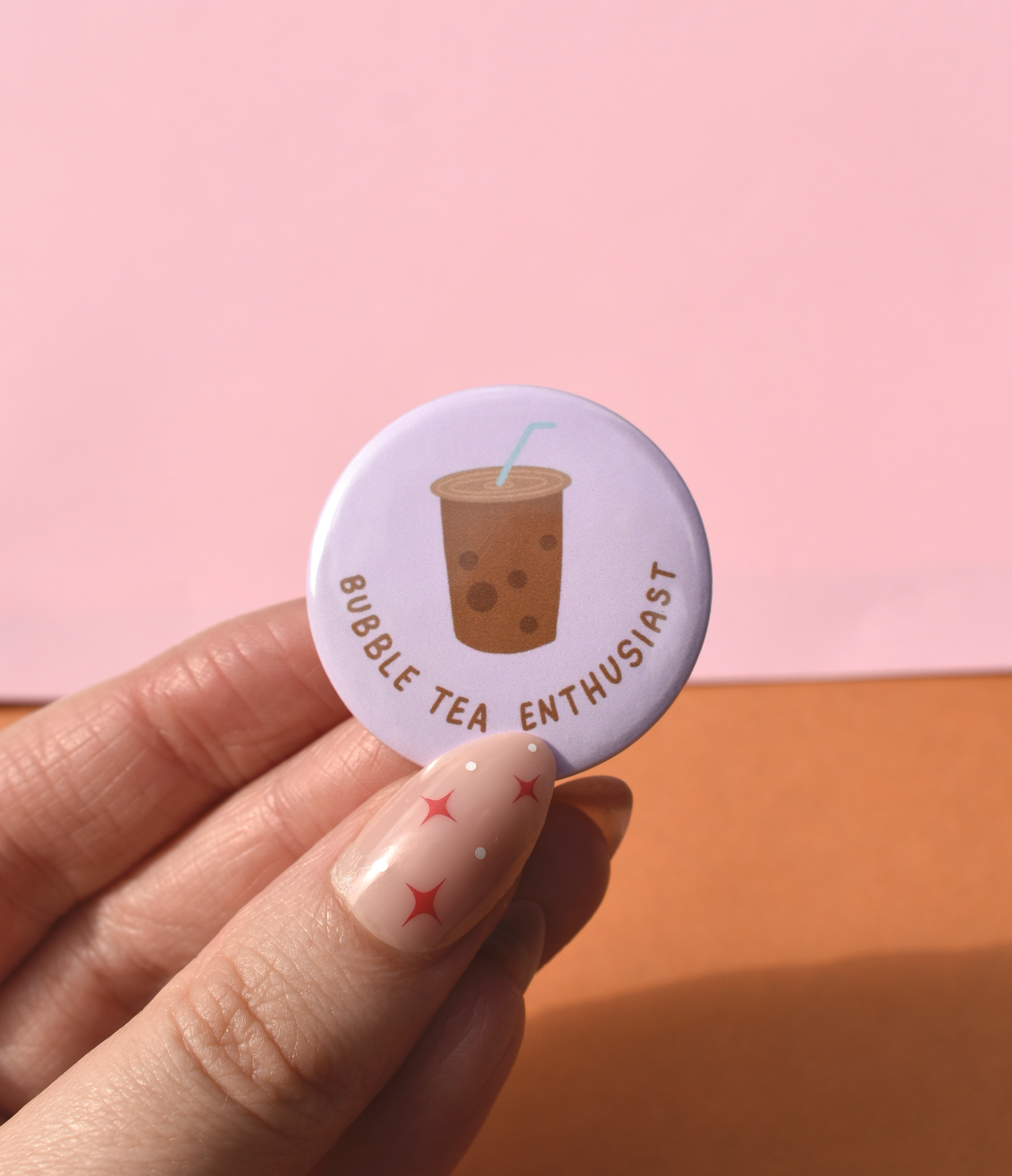 Button badge with bubble tea illustration and text held by a hand against a pink background