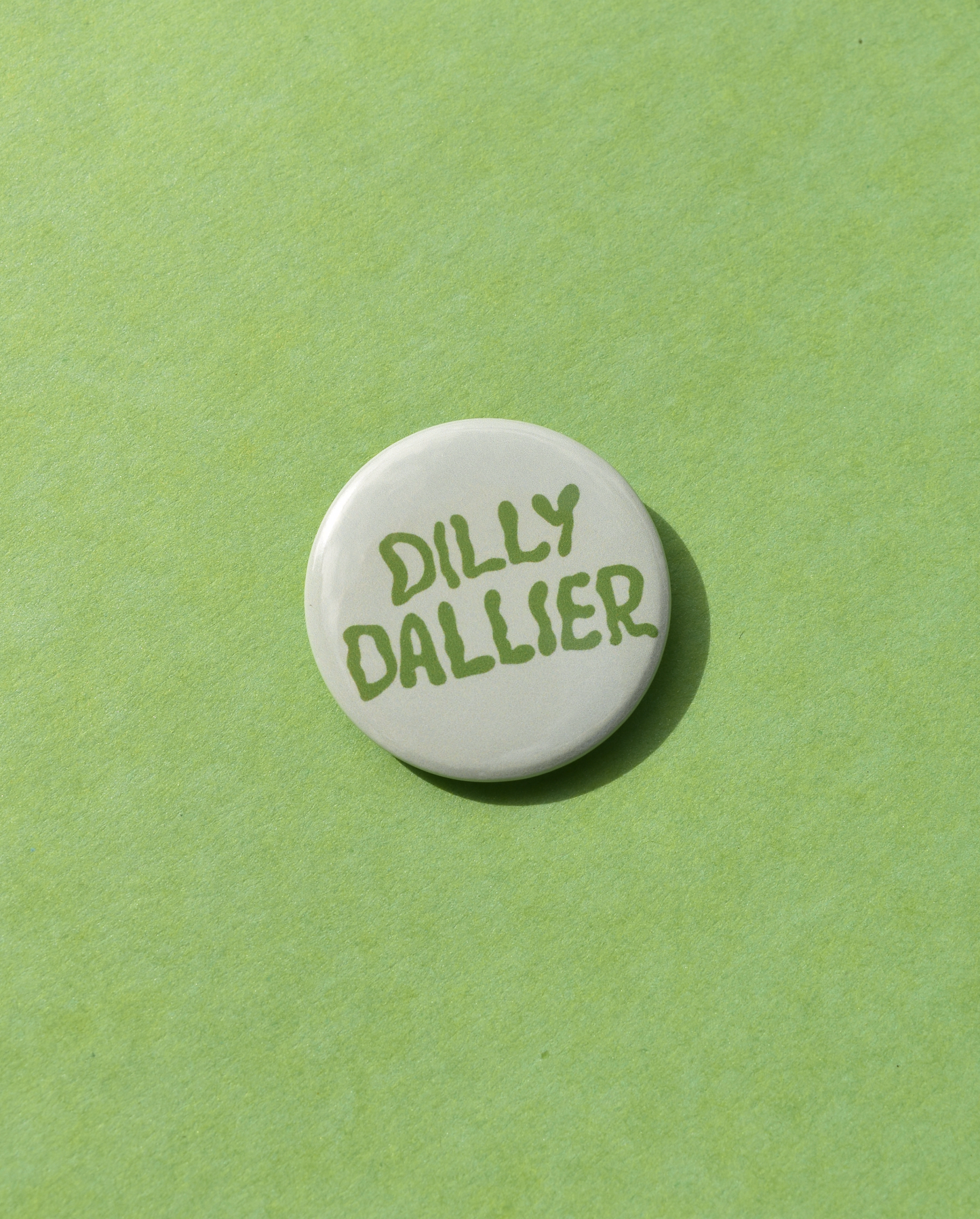 Round white button with 'Dilly Dallier' text on a green background