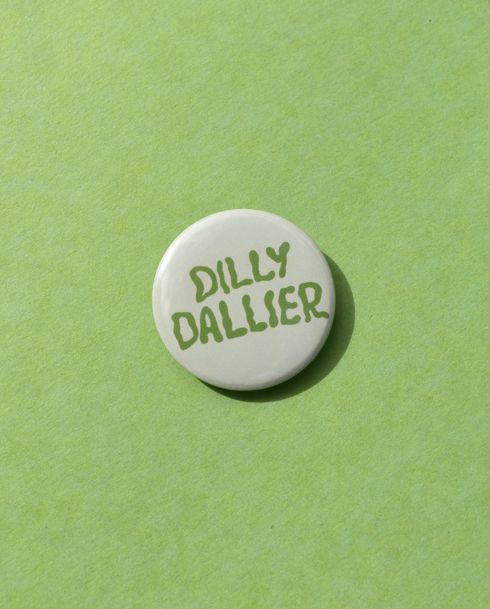 Round white button with 'Dilly Dallier' text on a green background