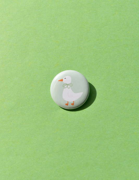 Round button with a cartoon duck design on a green background