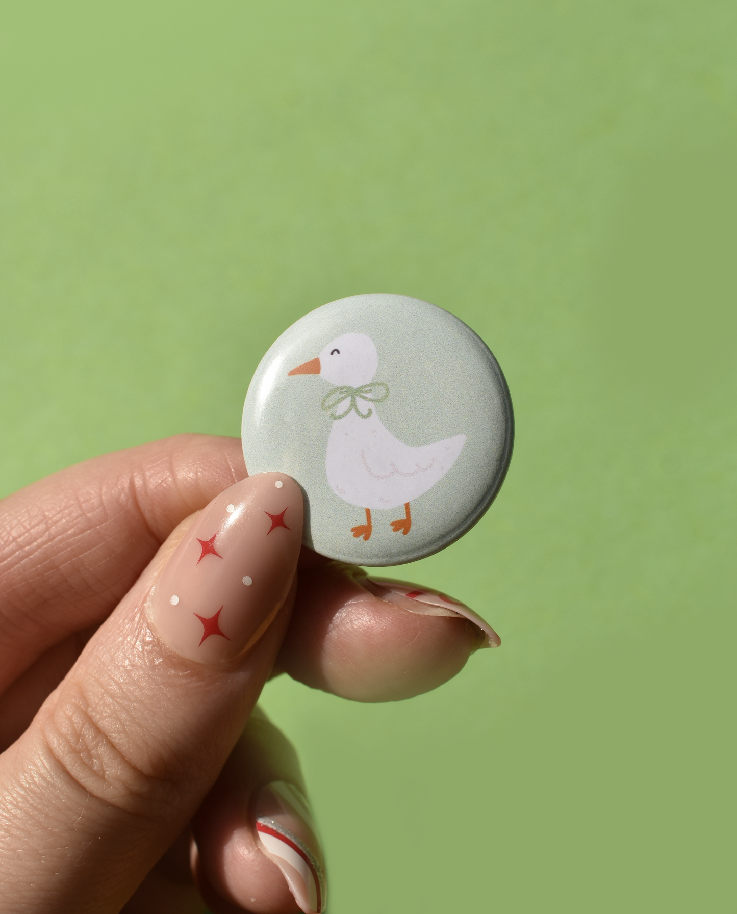 Button with a duck design held by a hand against a green background