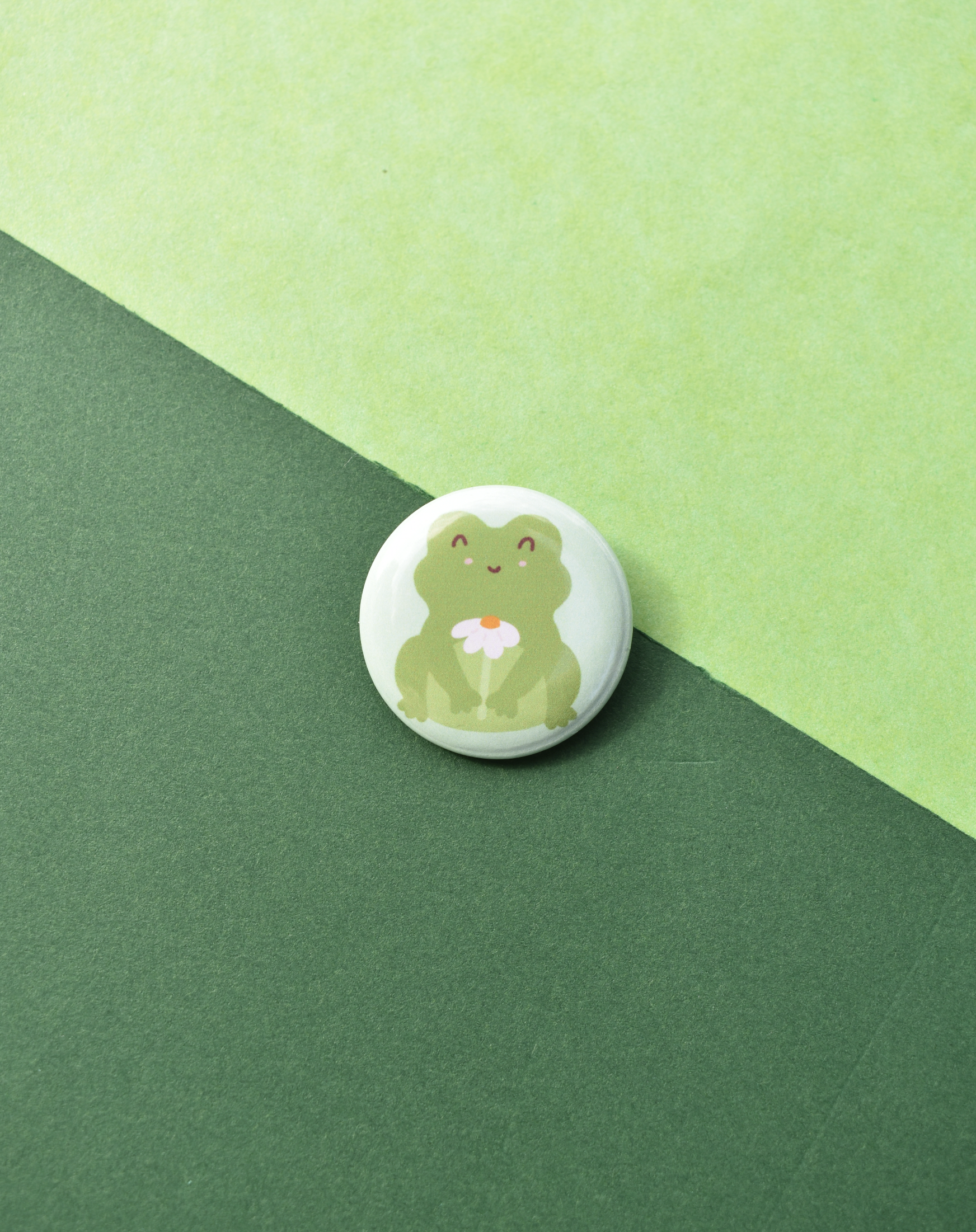 Button badge with a green frog holding a flower on a green background