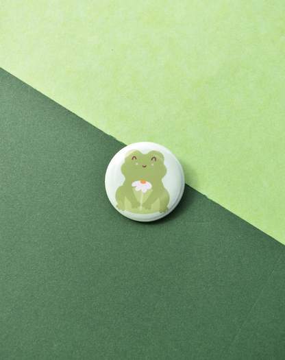 Button badge with a green frog holding a flower on a green background