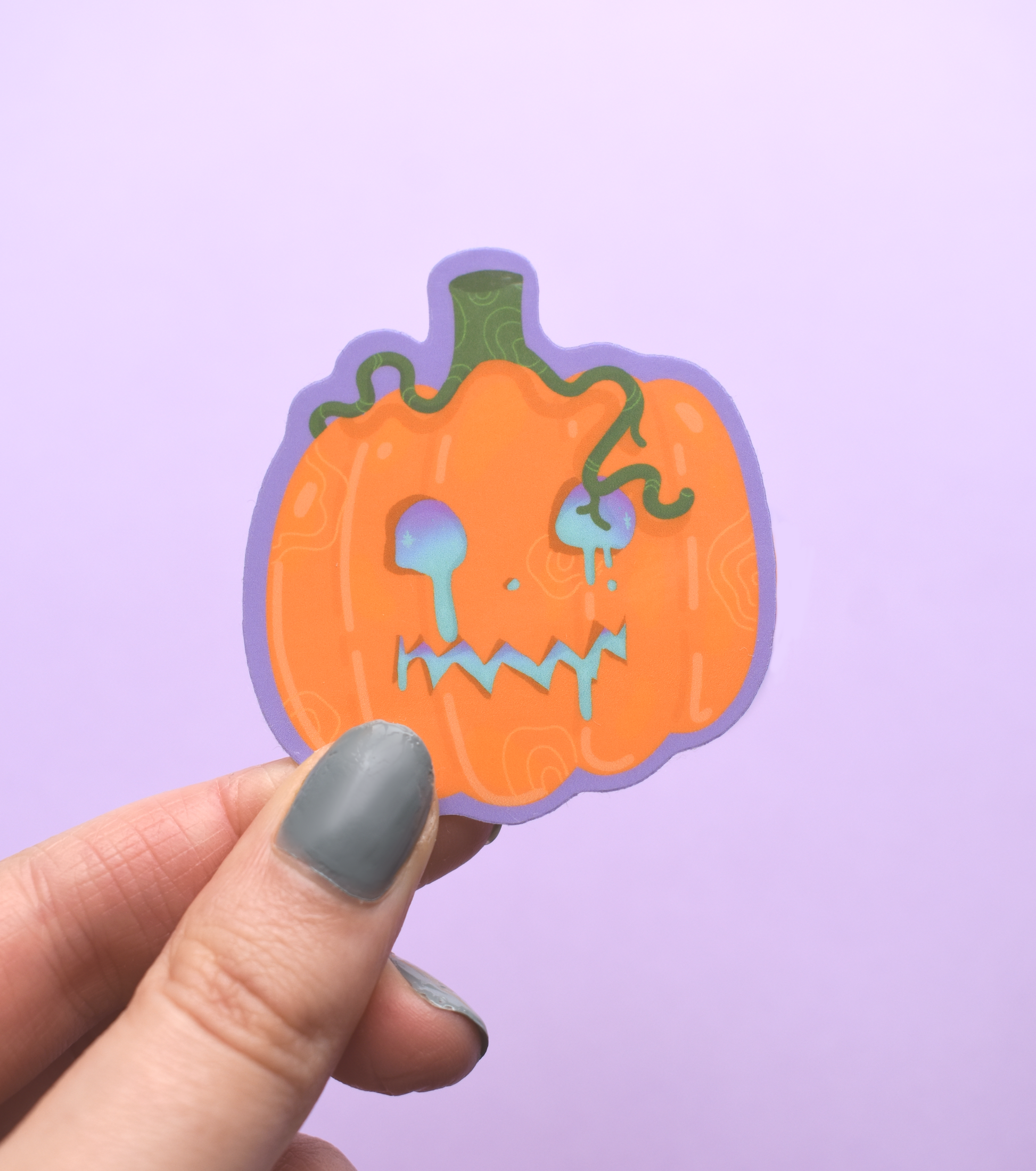 Hand holding a jack-o'-lantern sticker against a purple background