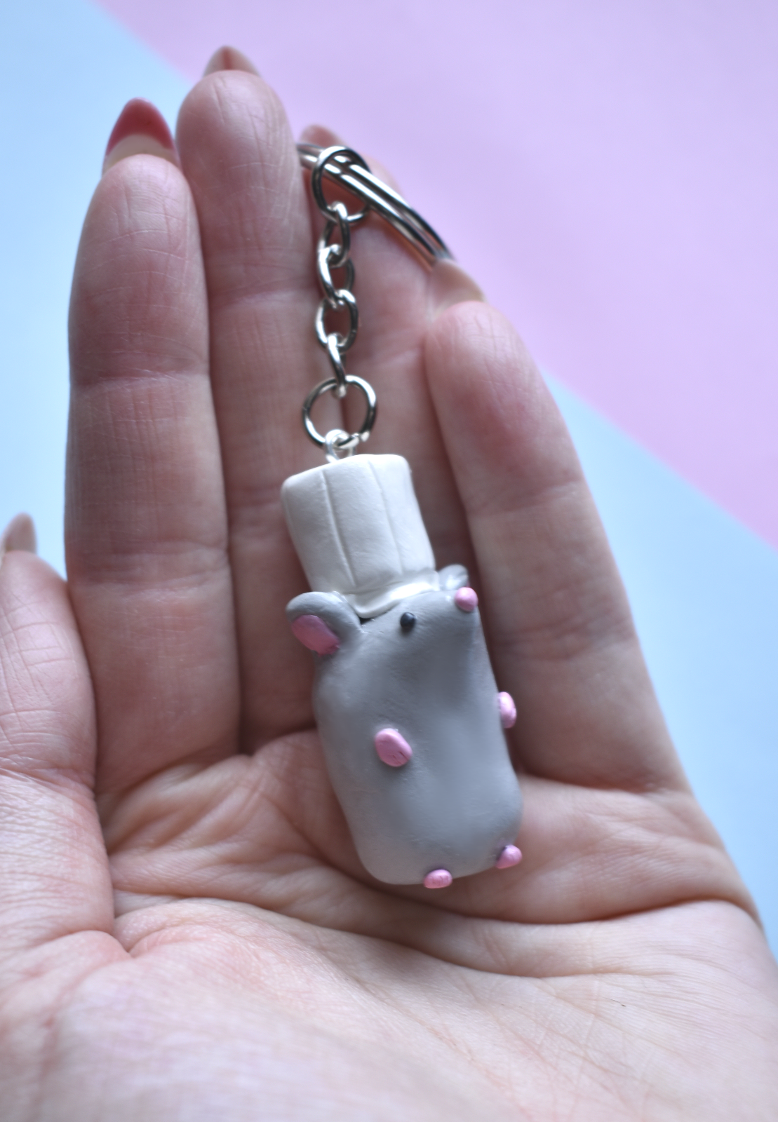 Hand holding a keychain with a small rat with a chef hat figure on a pink and blue gradient background