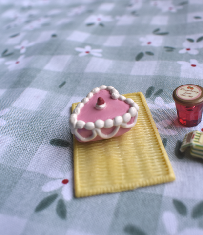 Small pink heart-shaped cake with white frosting on a yellow plate on a floral tablecloth.