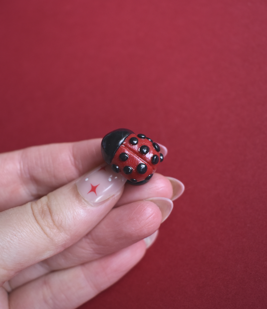 Small red and black ladybug pin held between fingers against a red background
