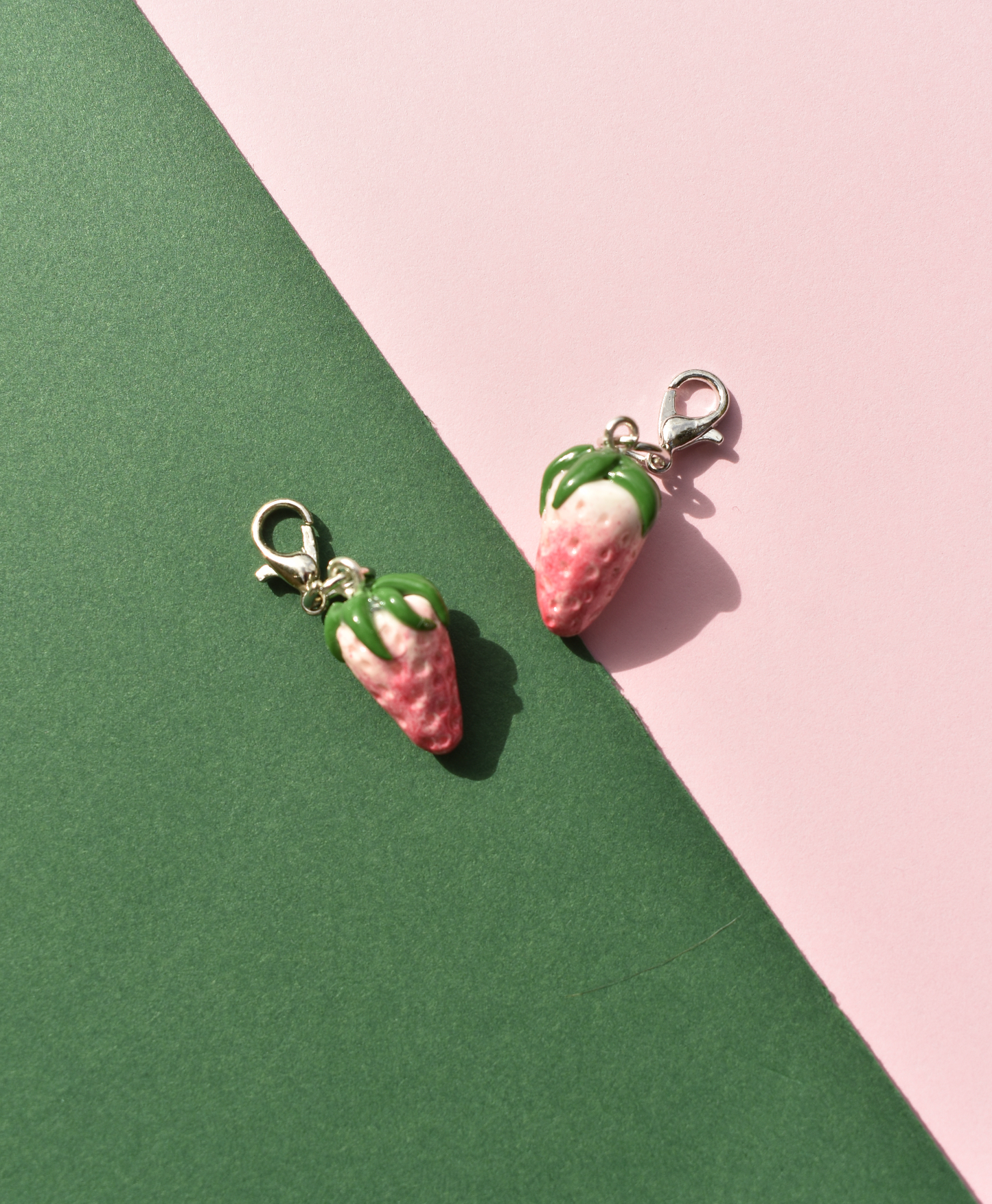 Two strawberry-shaped charms on a pink and green background