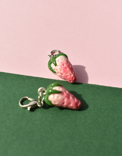 Two strawberry-shaped charms on a pink and green background