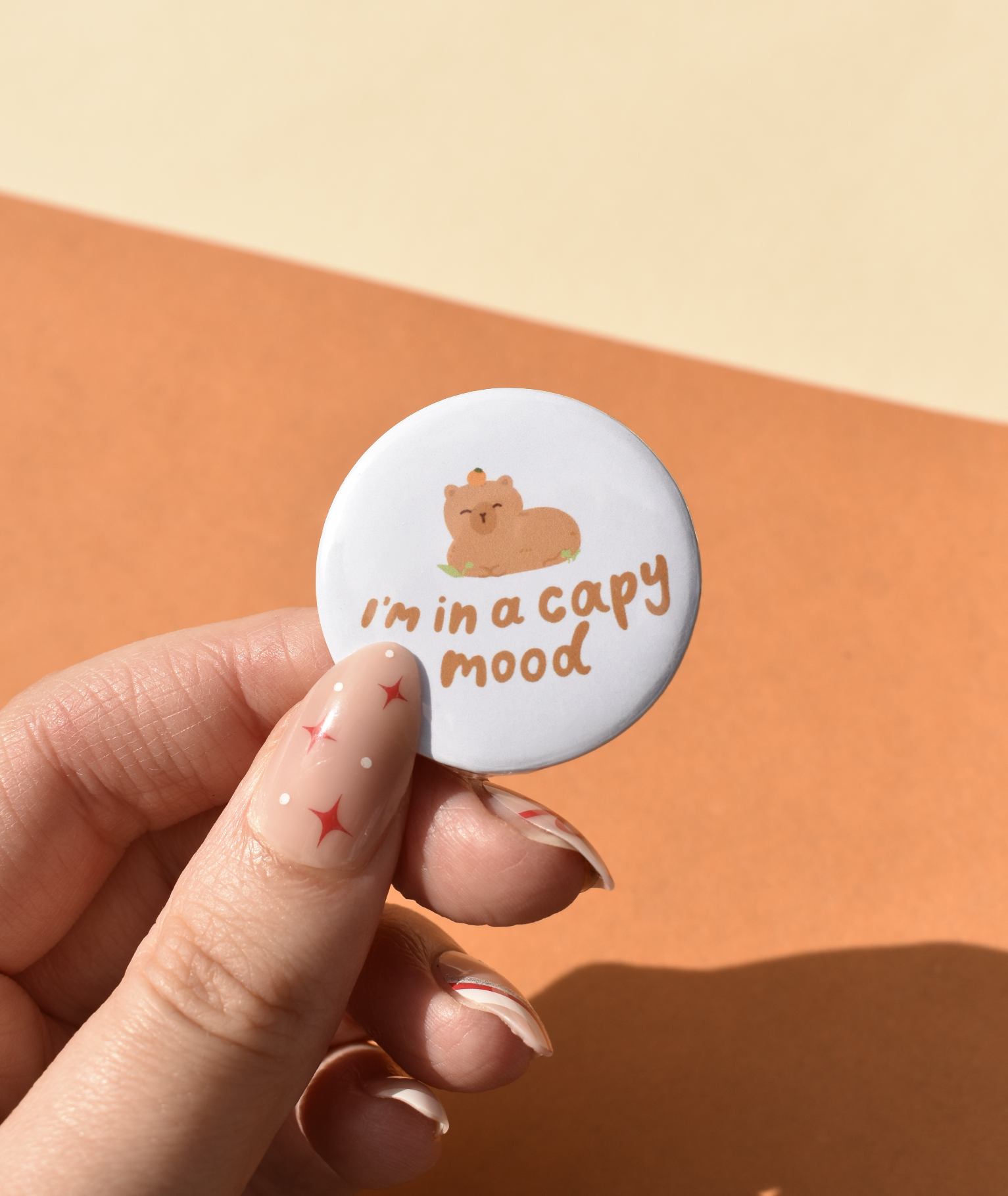Button badge with a cat illustration and text 'I'm in a capy mood' held by a hand against a two-tone background.