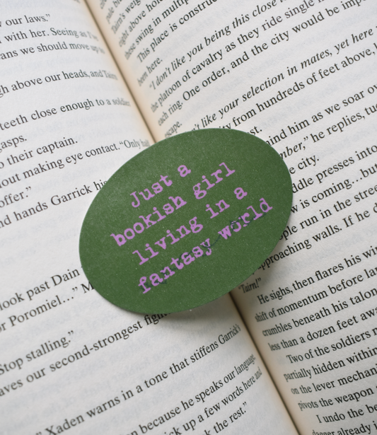 Green circular sticker with 'Just a girl in a bookish living fantasy world' text on an open book.