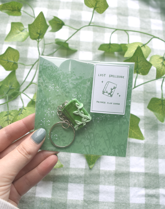 Green keychain with packaging held by a hand against a green and white checkered background