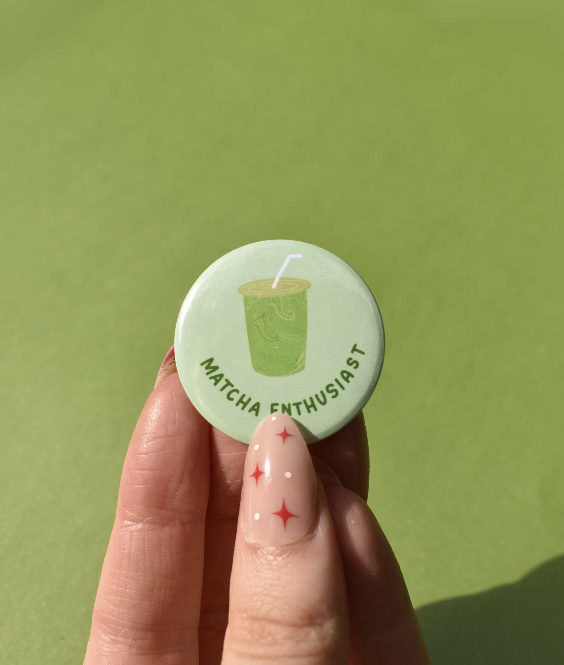 Button badge with 'Matcha Enthusiast' text and matcha graphic held by a hand against a green background
