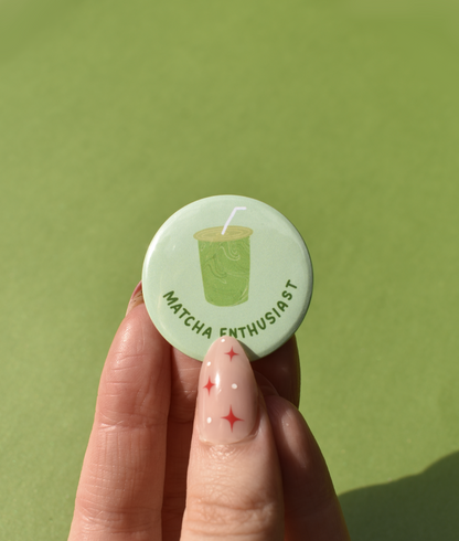 Button badge with 'Matcha Enthusiast' text and matcha graphic held by a hand against a green background