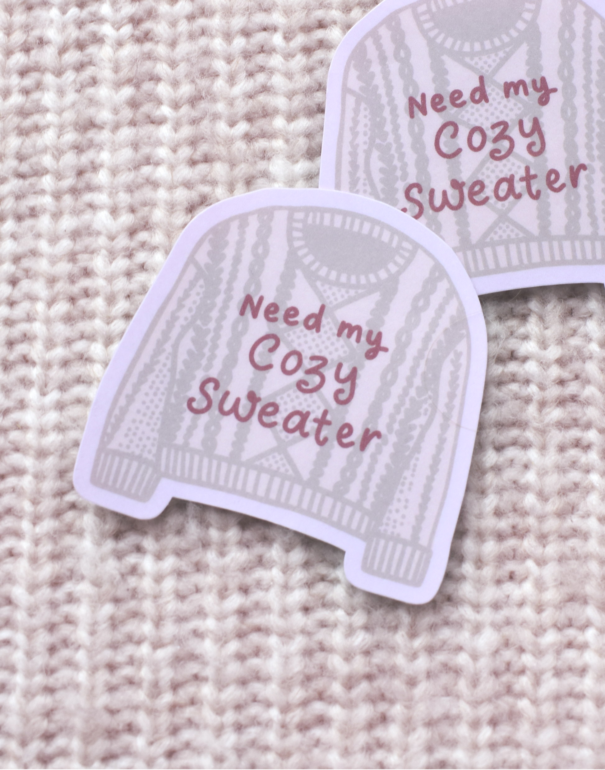 Two sweater stickers with 'Need my Cozy Sweater' text on a knitted background.