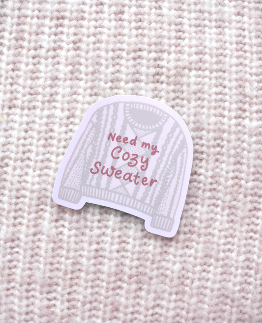 Knitted sweater with 'Need my Cozy Sweater' text on a textured beige background