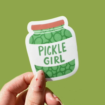 Pickle girl sticker held up by a hand on a green background 
