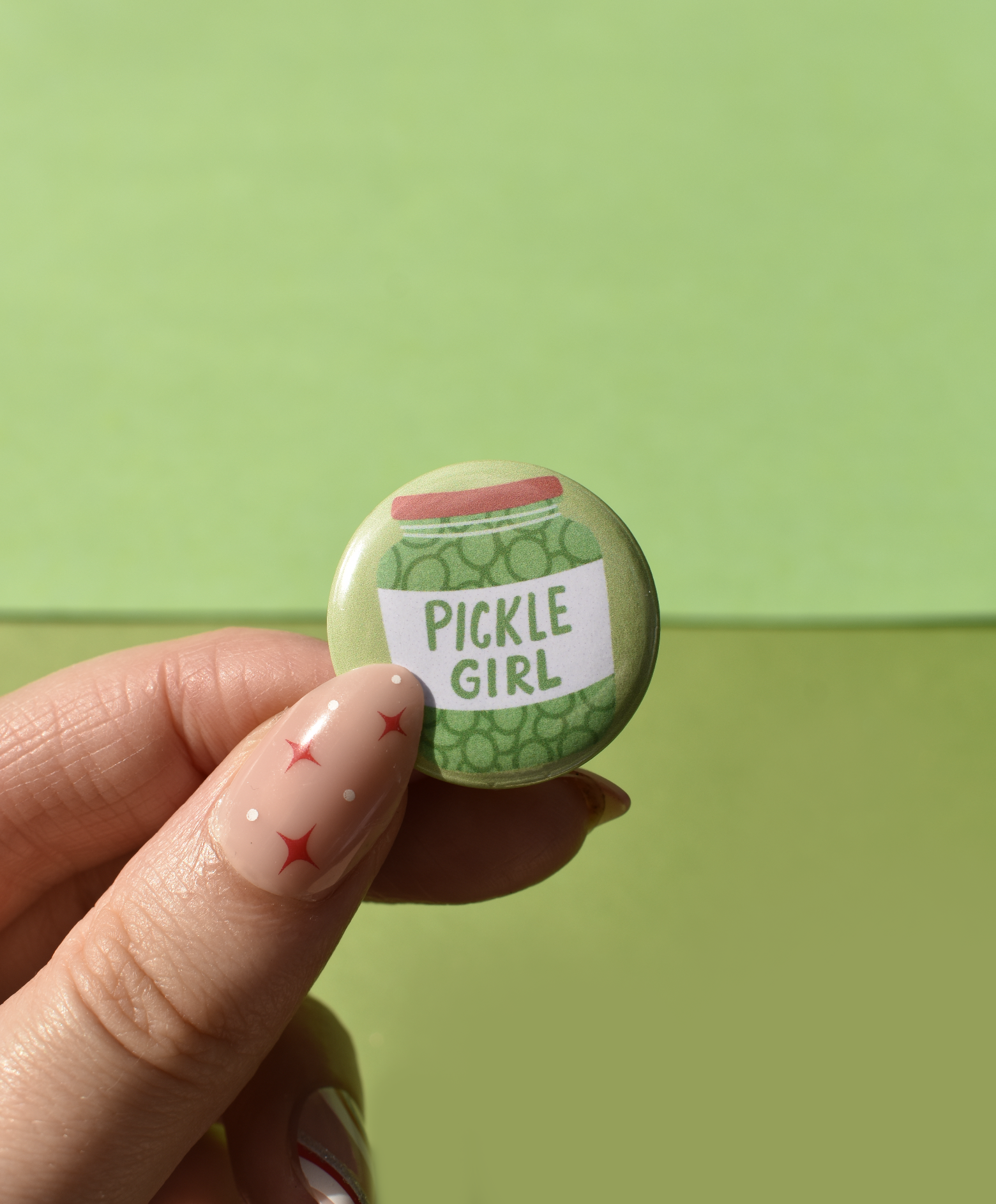 Button badge with 'Pickle Girl' text held by a hand against a green background