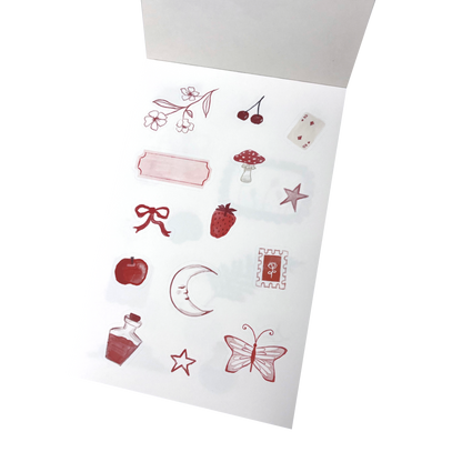 A sheet of decorative stickers with red and pink illustrations, including cherries, a strawberry, a mushroom, a bow, a crescent moon, stars, a butterfly, and a small bottle.