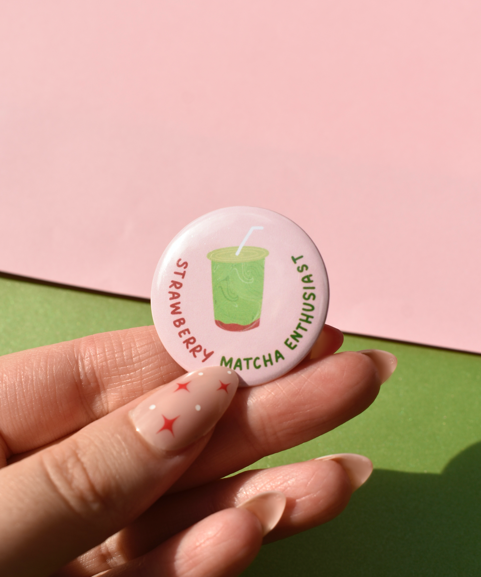 Button badge with 'Strawberry Matcha Enthusiast' text held by a hand on a pink and green background