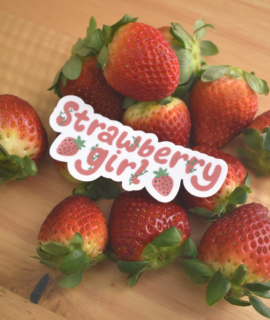 Strawberries on a wooden surface with a 'Strawberry girl' sticker.
