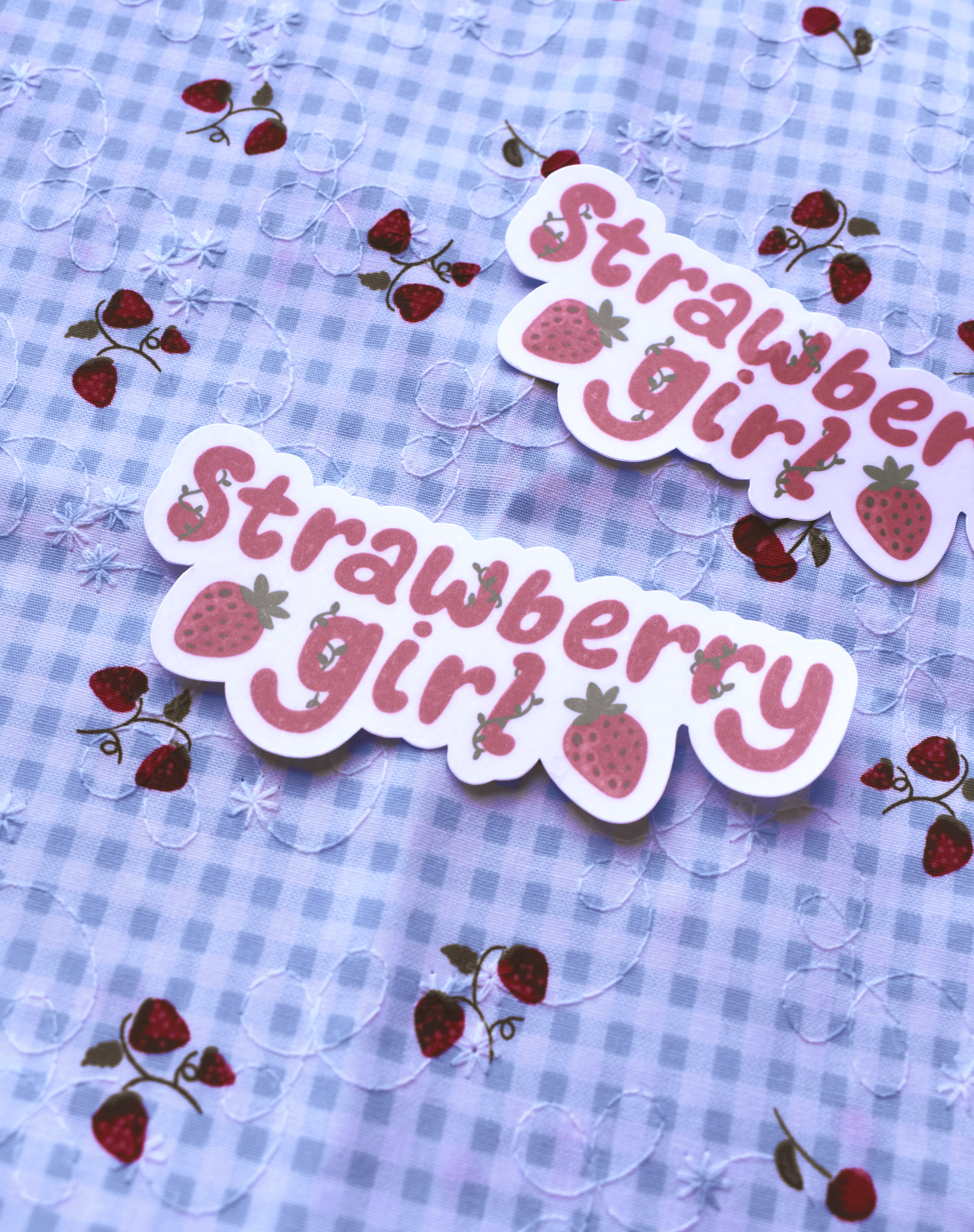Two 'Strawberry girl' stickers on a blue checkered background with strawberry designs.