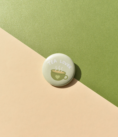 Round button badge with 'Tea Lover' text and tea cup illustration on a green and beige background