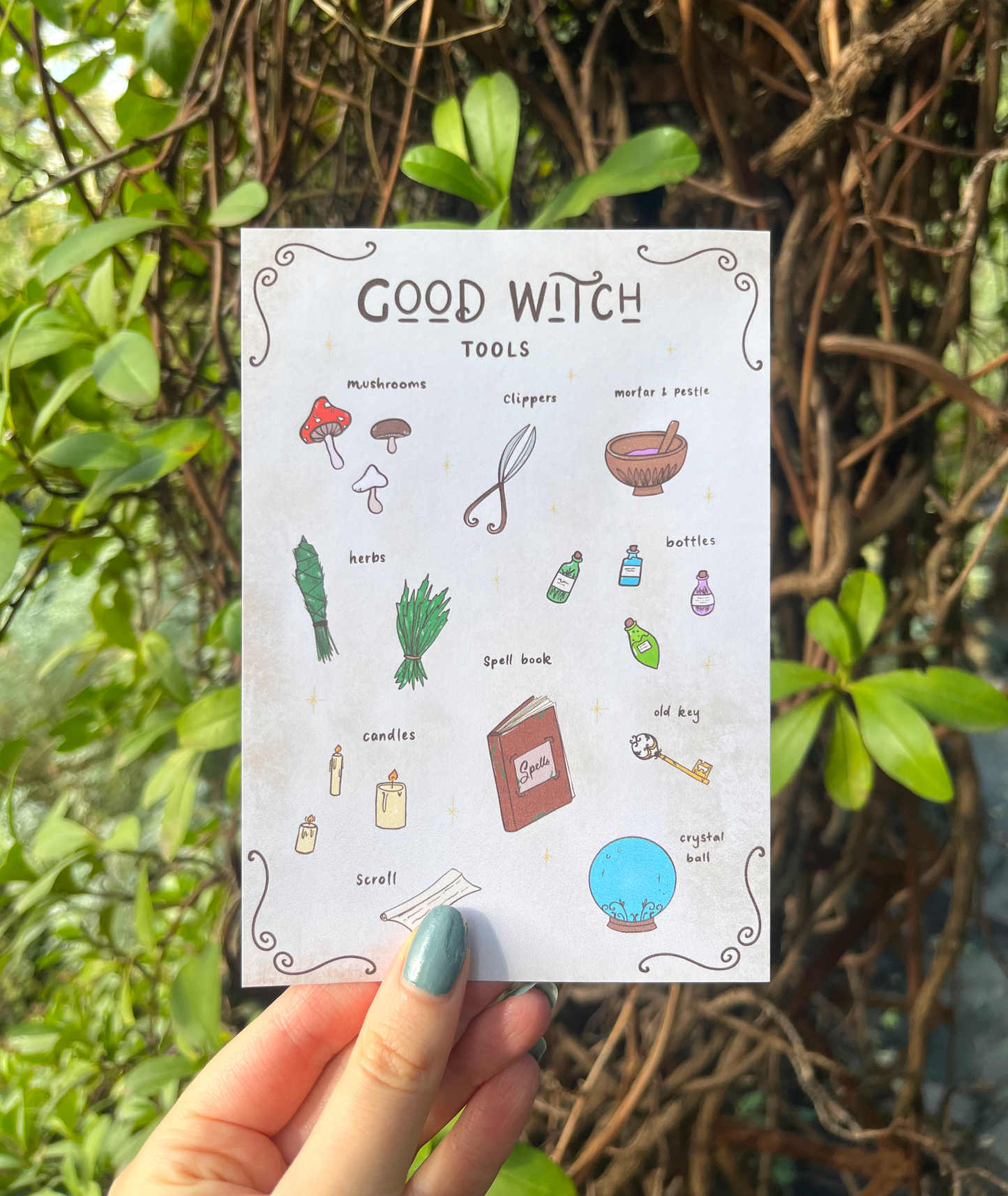 Hand holding a card titled 'Good Witch Tools' with illustrations of various items against a natural background.