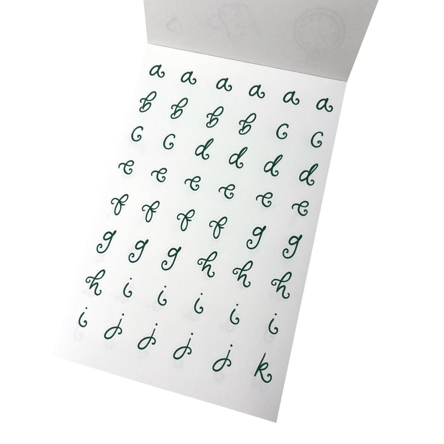 A white sheet of alphabet stickers showing lowercase cursive letters from a to k in dark green. 