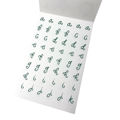 A white sheet of alphabet stickers showing lowercase cursive letters from a to k in dark green. 