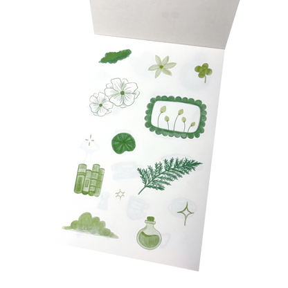 A sheet of botanical-themed stickers featuring green and white illustrations of flowers, leaves, a fern, a clover, a small potion bottle, and decorative frames.
