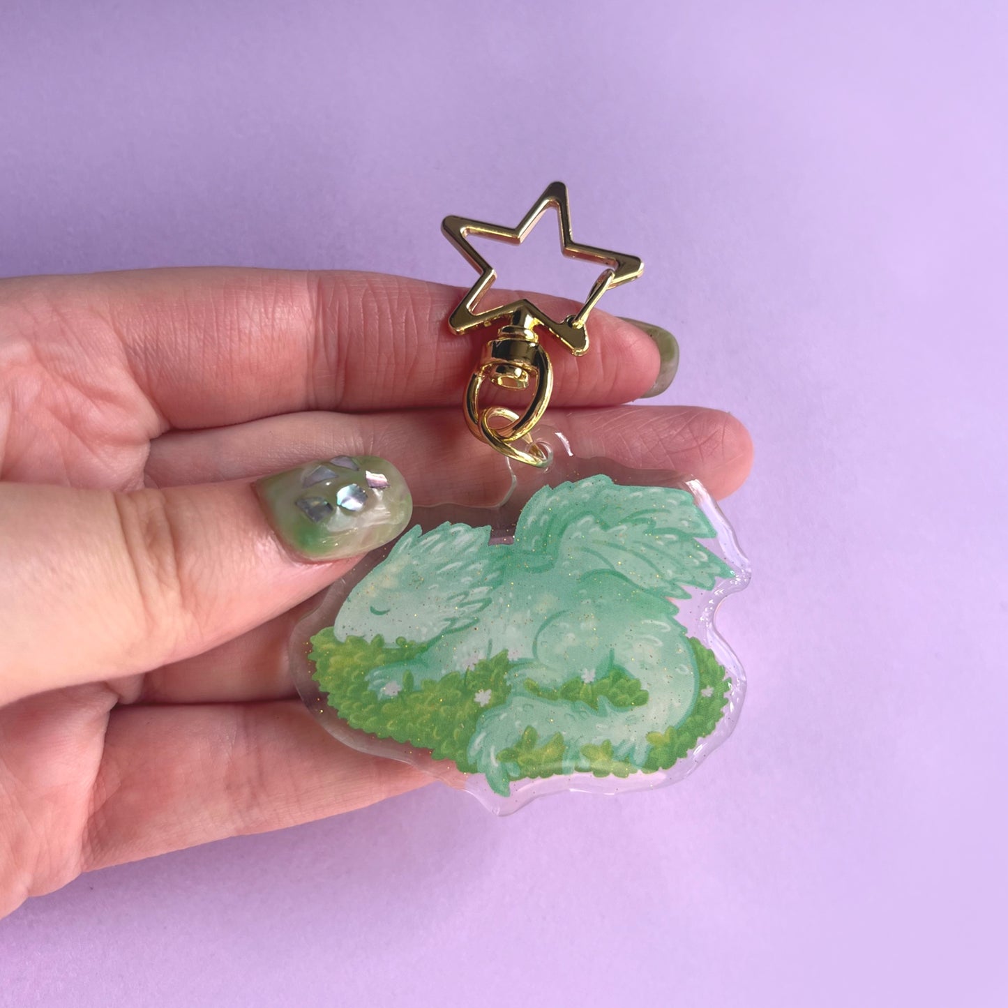 Close-up of sleeping baby dragon acrylic keychain showing glitter finish and leafy details