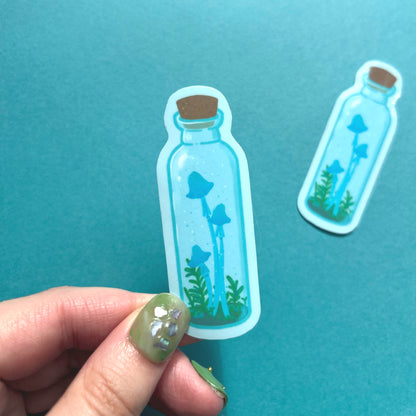 Whimsical fantasy sticker featuring blue mushrooms inside a clear potion bottle with greenery