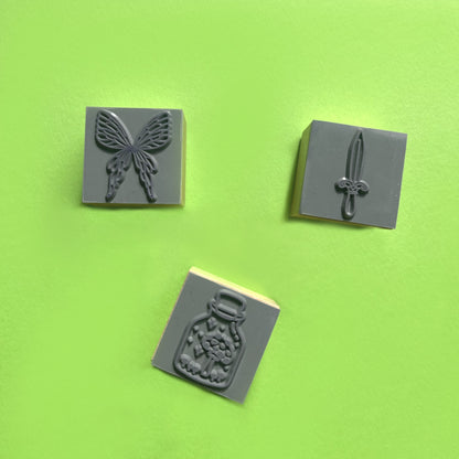 Close-up of fantasy rubber stamps showing fairy wings sword and mushroom in jar details