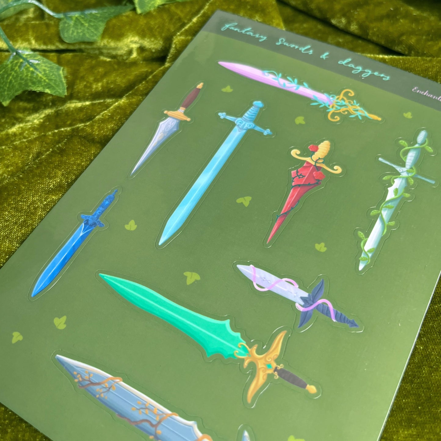 Close-up of glossy fantasy sword and dagger stickers showing detailed colourful weapon designs