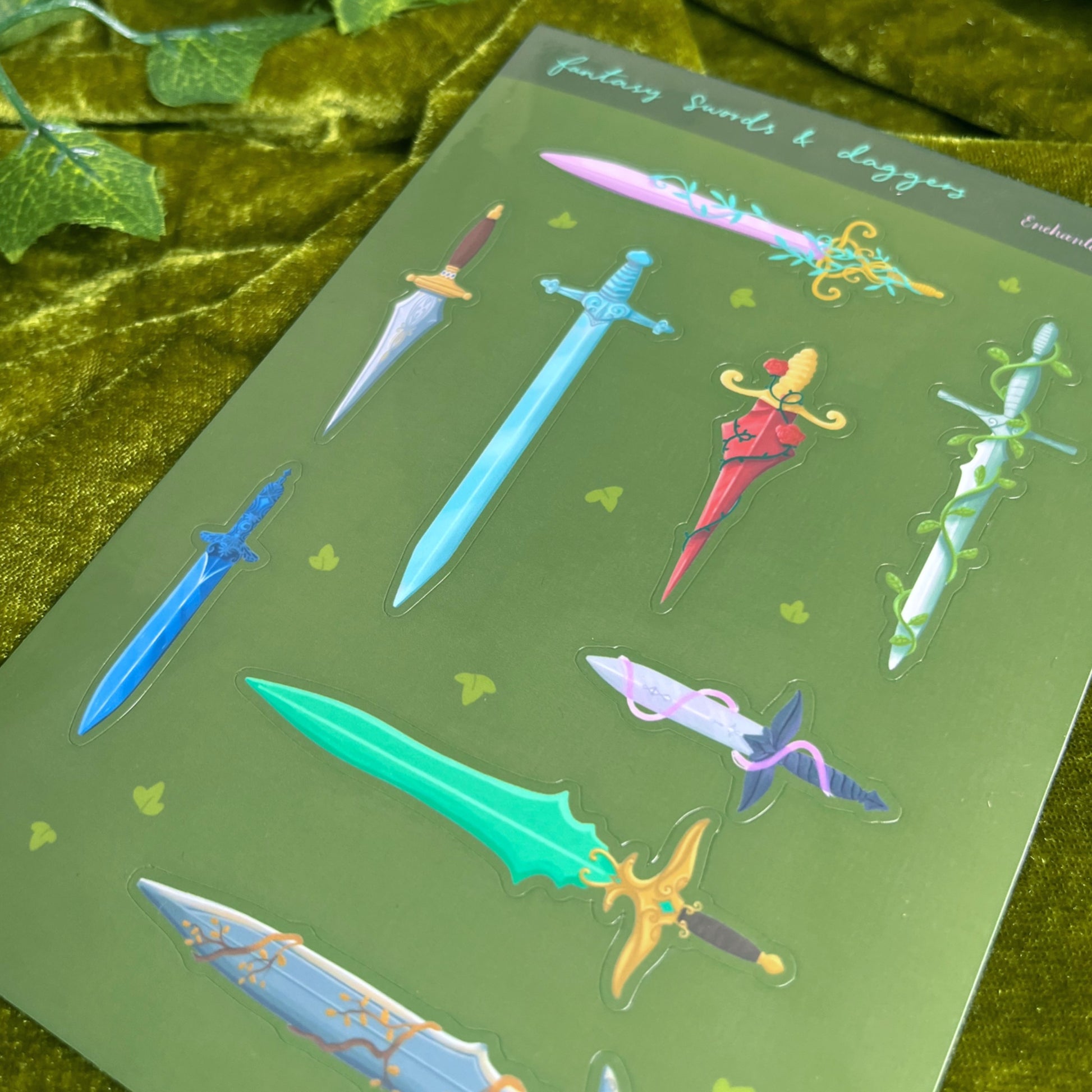 Close-up of glossy fantasy sword and dagger stickers showing detailed colourful weapon designs