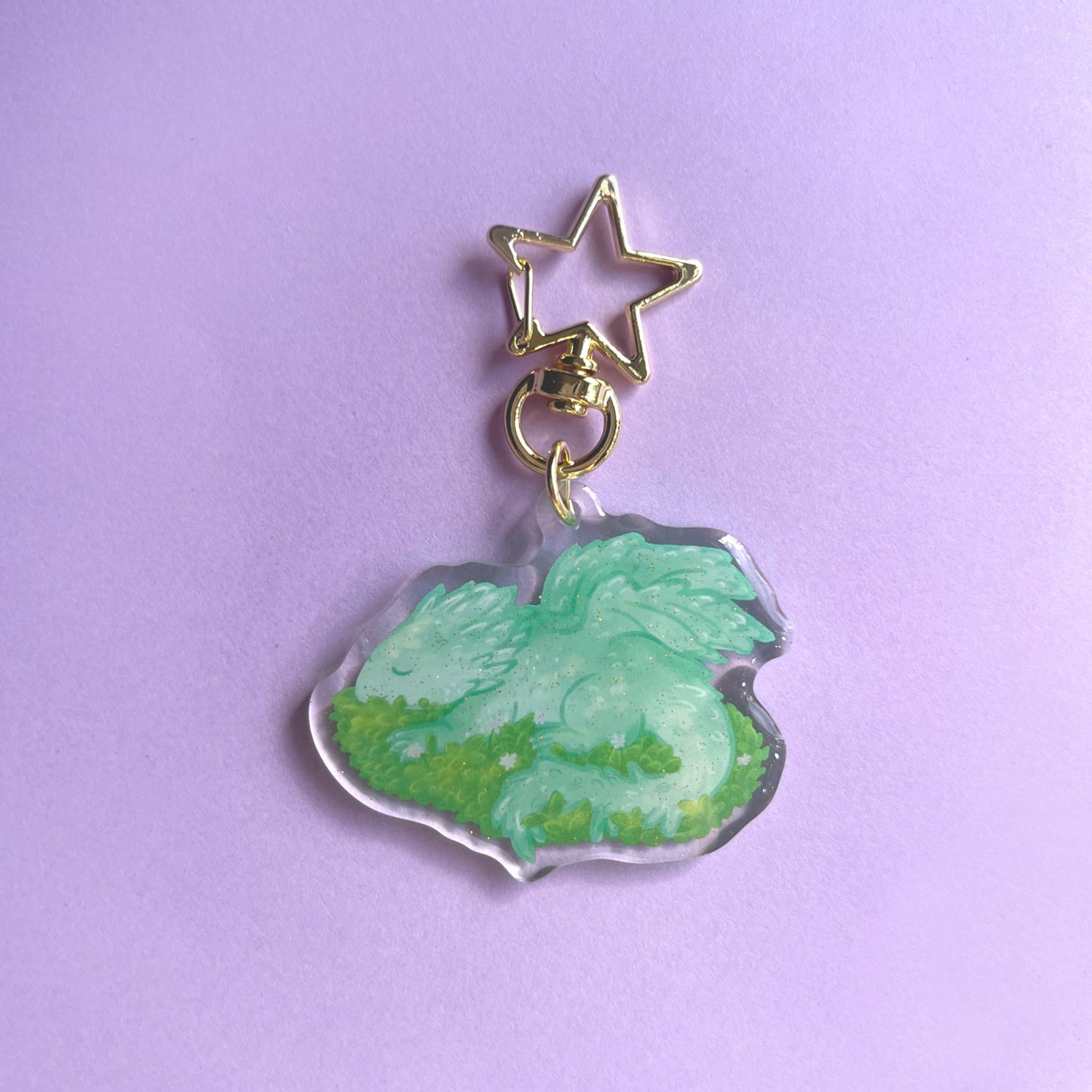 Sleeping baby dragon acrylic keychain with glitter finish featuring light green dragon on leaves
