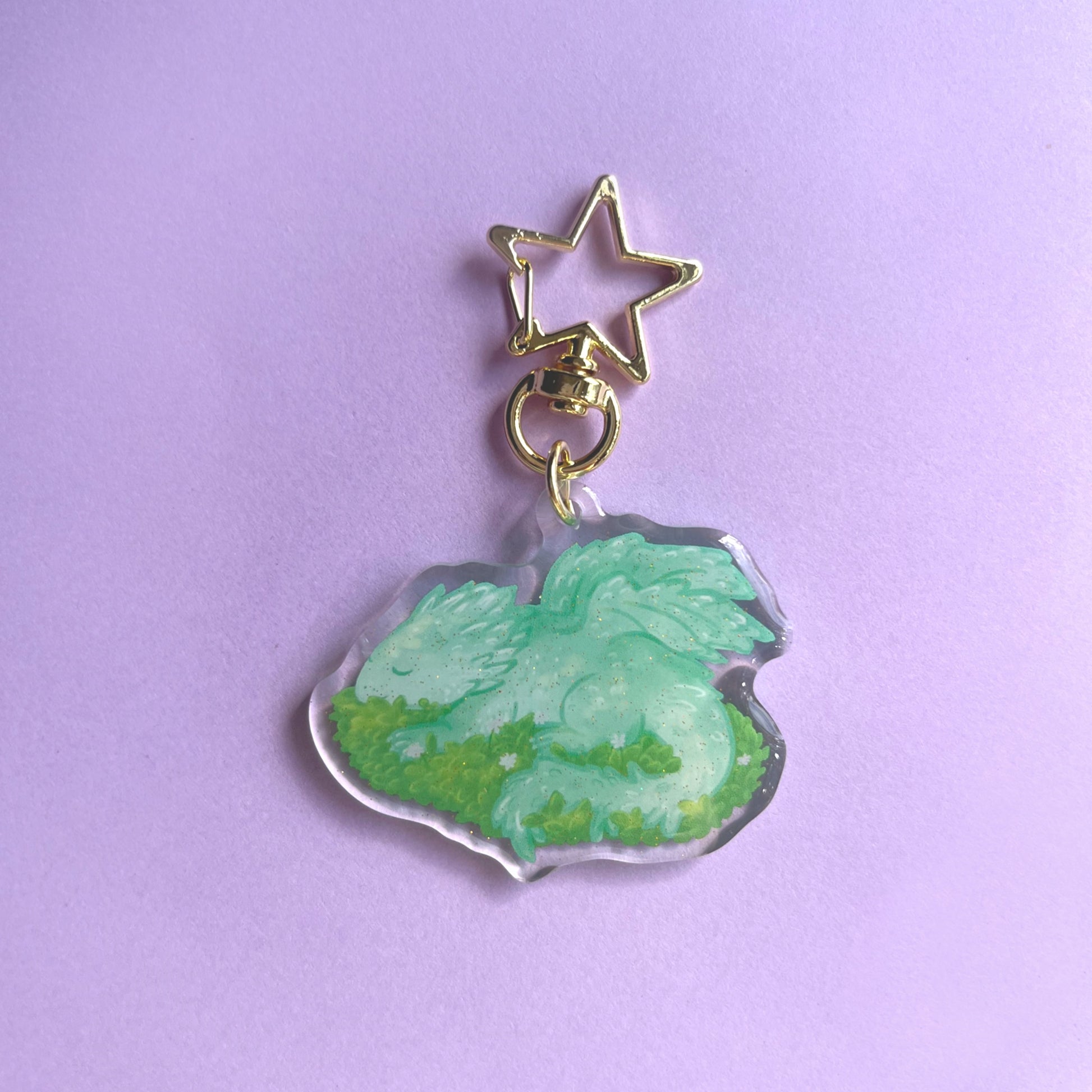 Sleeping baby dragon acrylic keychain with glitter finish featuring light green dragon on leaves