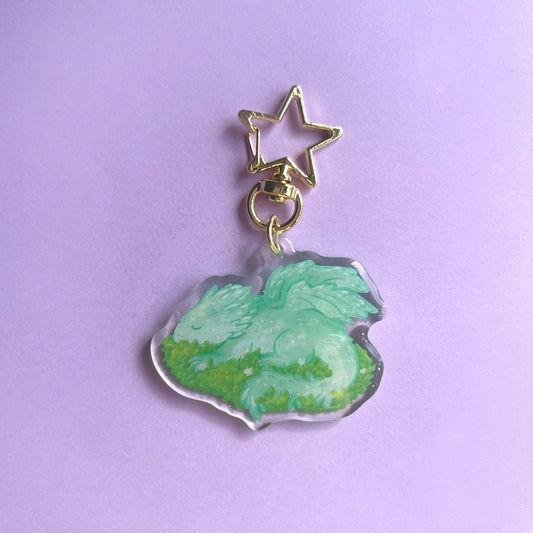 Sleeping baby dragon acrylic keychain with glitter finish featuring light green dragon on leaves