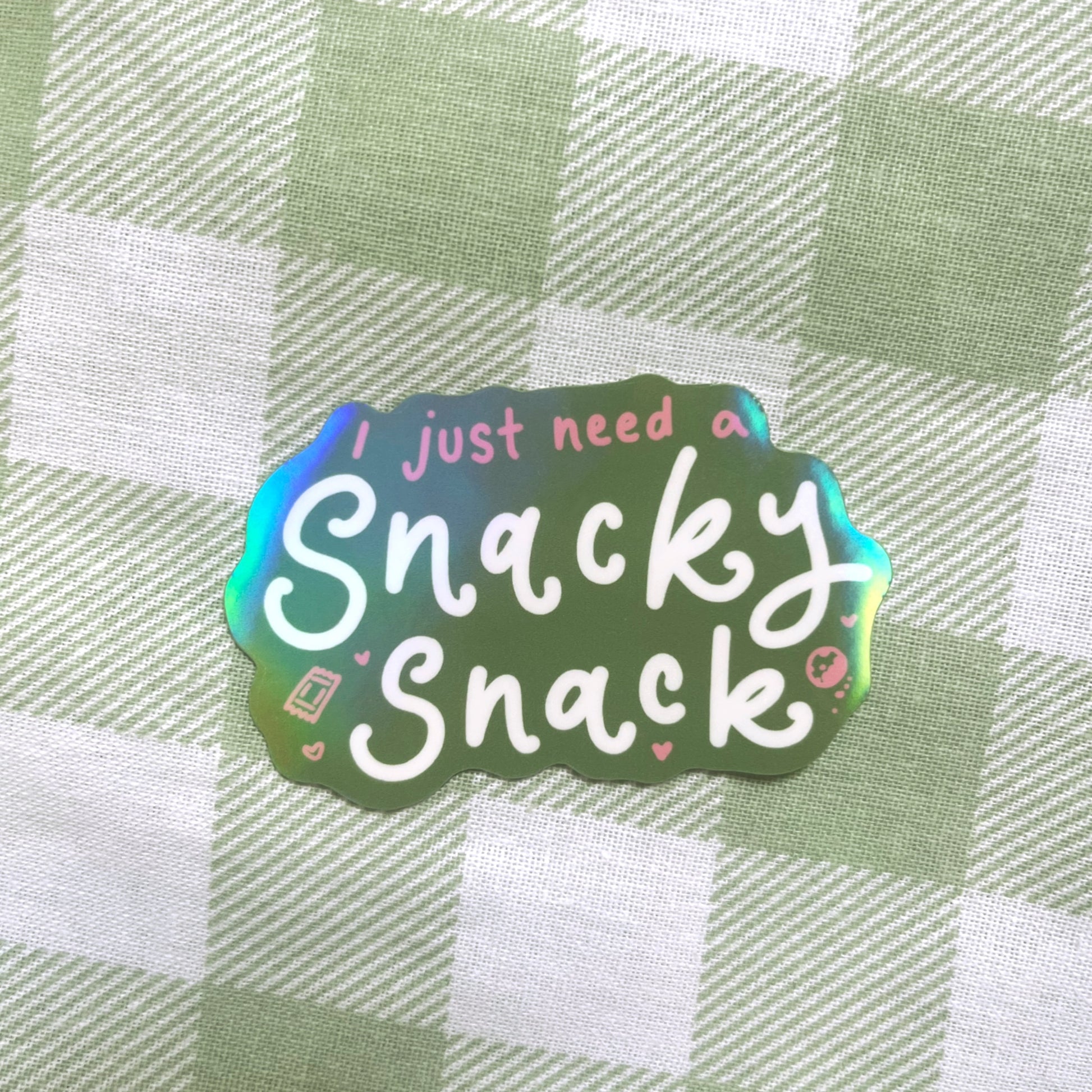 Holographic sticker with 'I just need a Snacky Snack' text on a green and white checkered background